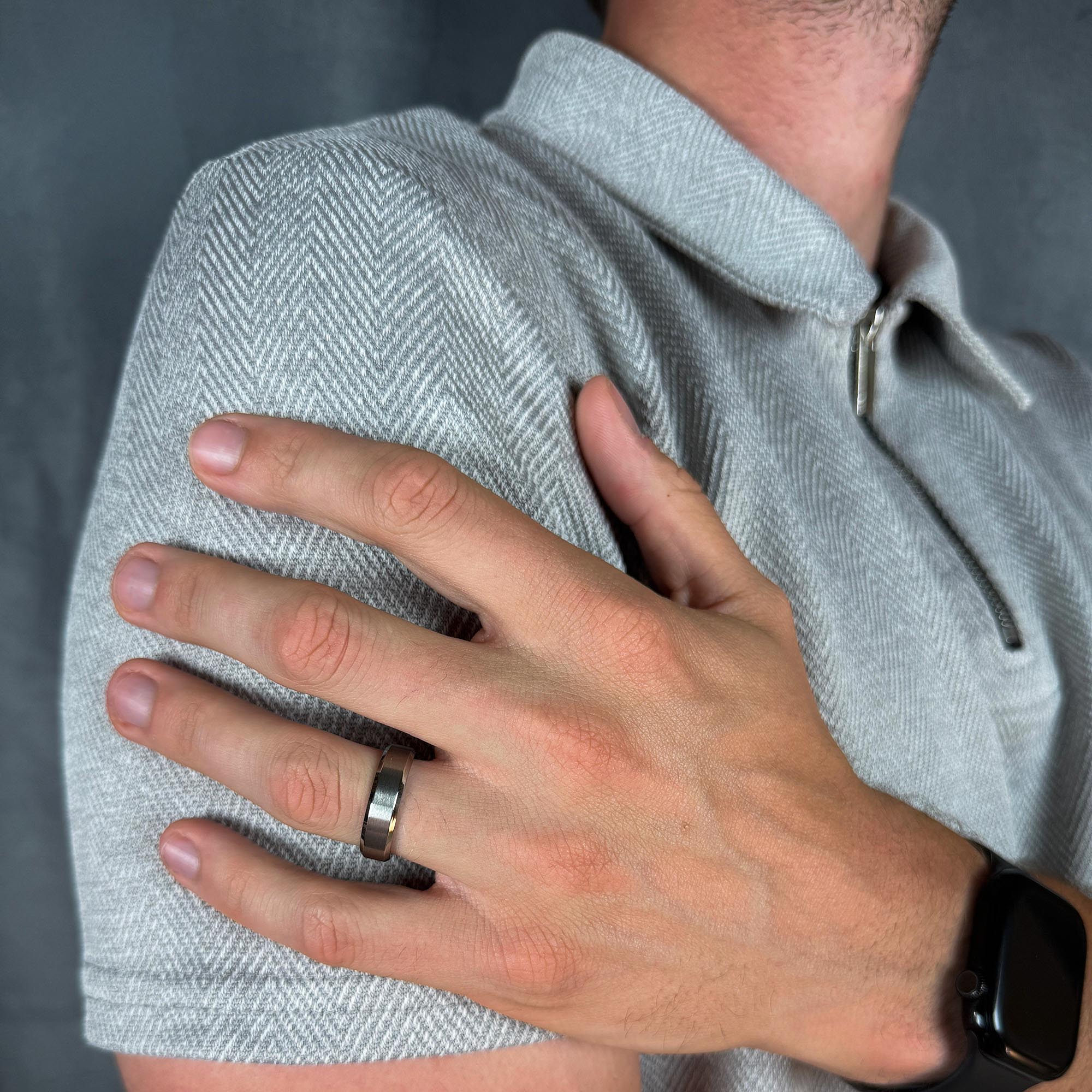 Person wearing a gray shirt jacket with a hand on their shoulder, wearing a silver ring.