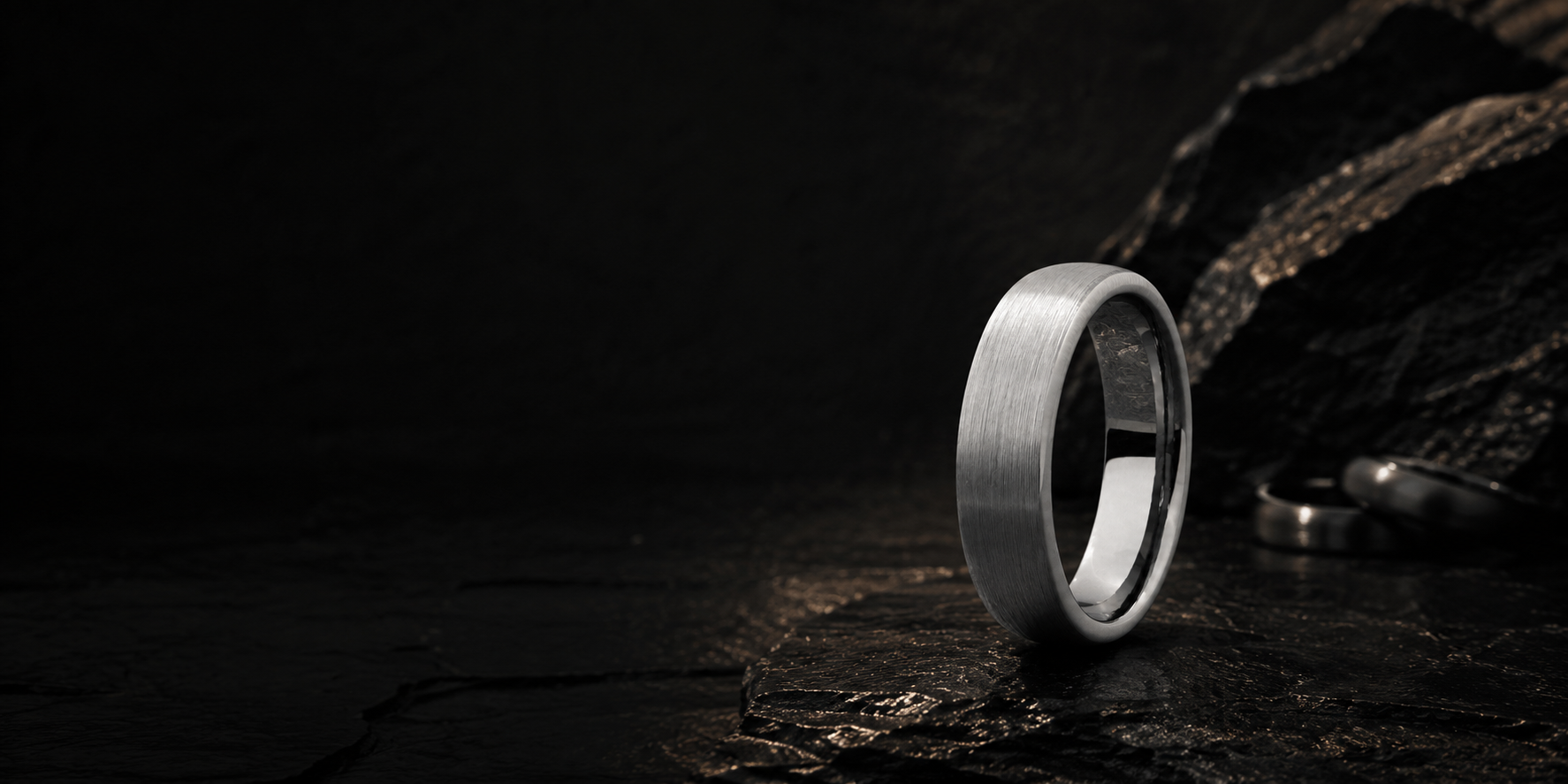 Close-up brushed silver tungsten wedding ring on dark slate stone with polished edges and rugged masculine styling