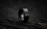 Matte black men’s wedding band on rugged dark stone for the HusBands men’s wedding bands collection.