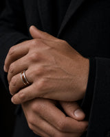 Man wearing a silver and reddish-brown wood inlay ring with a dark tailored jacket.