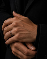 Man wearing a silver and reddish-brown wood inlay ring with a dark tailored jacket.