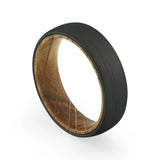 Angled view of a men's black tungsten wedding band with a real whiskey barrel wood inlay.