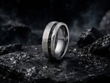 Silver faceted tungsten meteorite ring on dark volcanic rock with cinematic lighting and rugged charcoal textures