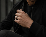 Man wearing a silver faceted meteorite tungsten wedding ring with black modern menswear styling in a moody urban lifestyle setting
