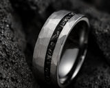 Ultra close-up macro photograph of a silver faceted meteorite tungsten ring showing detailed meteorite inlay texture and polished edges against dark volcanic stone background