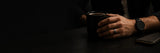 Modern minimalist men's wedding ring lifestyle banner featuring a silver wedding band, black coffee mug and contemporary accessories in a dark luxury setting.