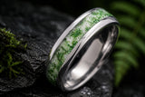 Ultra close-up macro photograph showing the detailed green moss agate inlay and polished silver tungsten edges of a luxury wedding ring resting on dark textured stone.