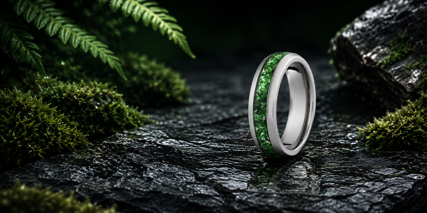 Wide desktop banner for moss agate wedding rings collection featuring a silver tungsten ring with natural green moss agate inlay positioned on a dark woodland-inspired luxury background.