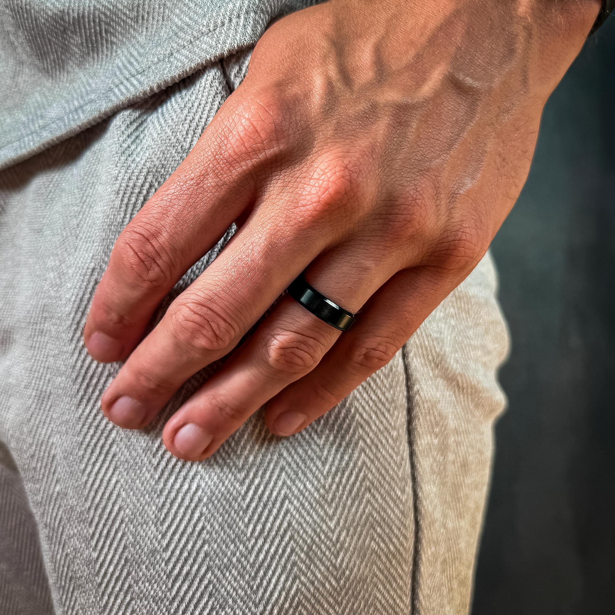 Hand wearing a black ring with a neutral background