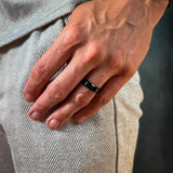 Hand wearing a black ring with a neutral background