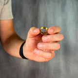 Hand holding a gold ring against a gray background