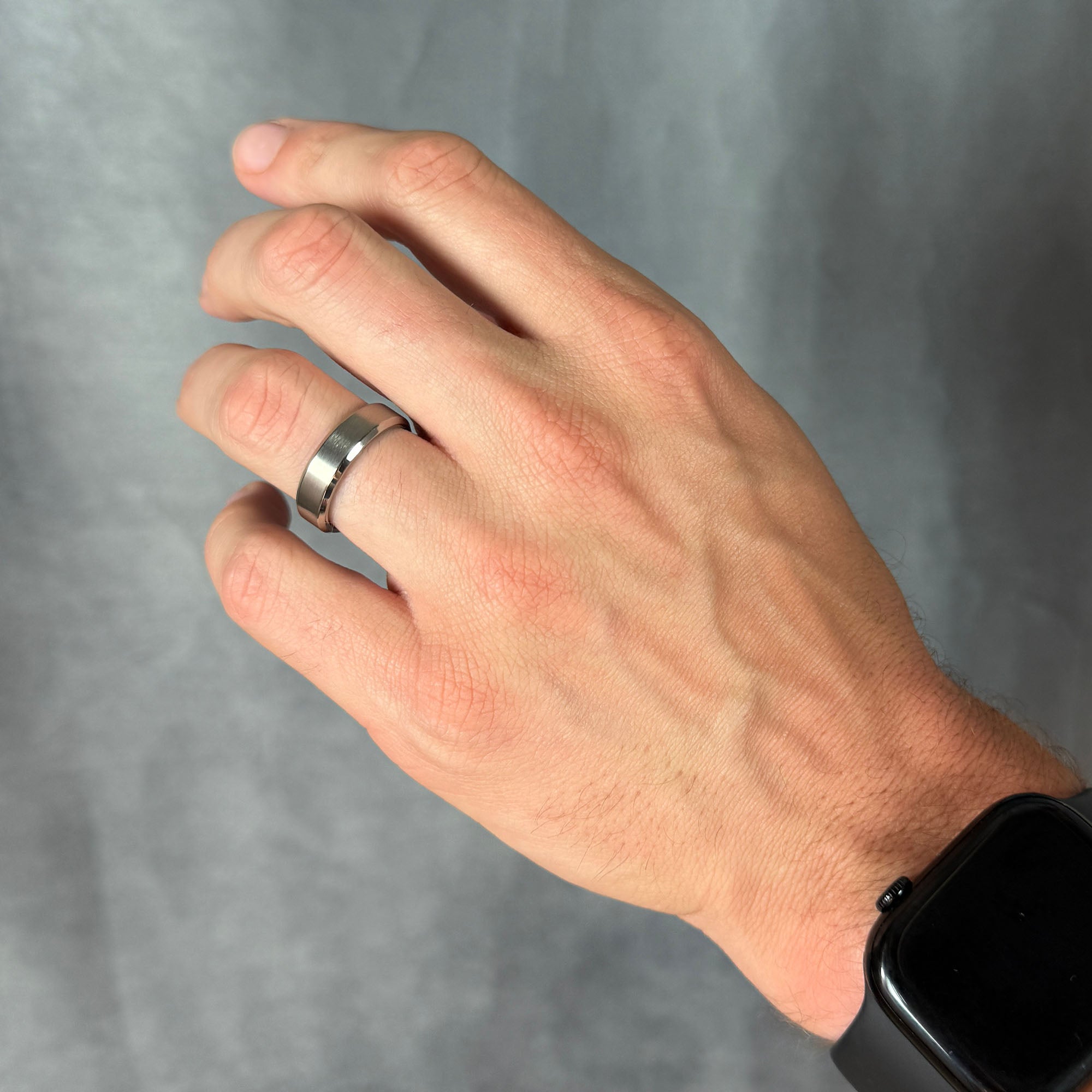 Hand wearing a silver ring on a gray background