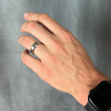 Hand wearing a silver ring on a gray background