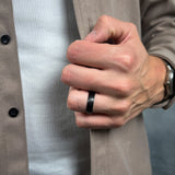 Hand wearing a black titanium ring with a blurred background