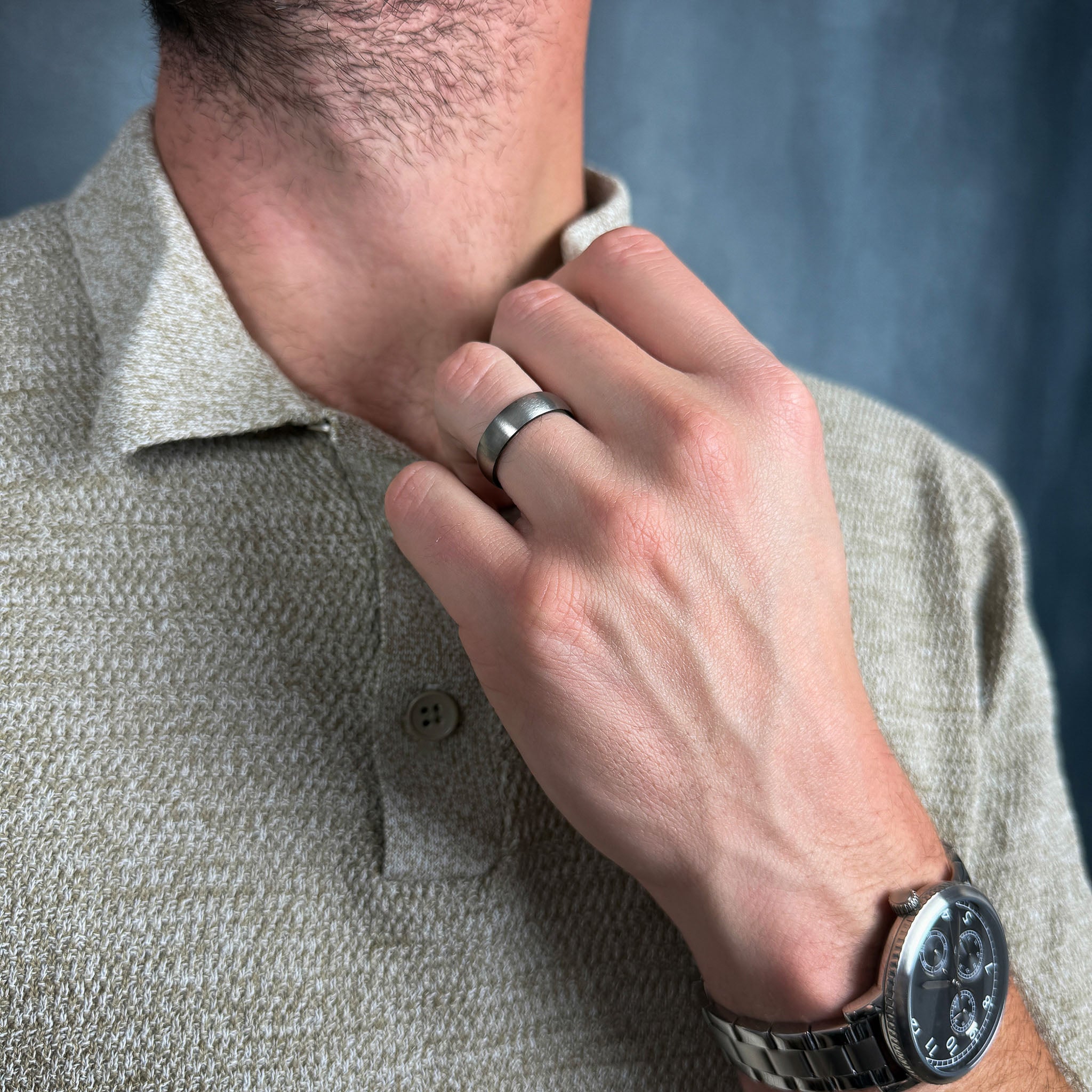 a man wearing a brushed silver titanium ring with a polished black inner sleeve holding his shirt collar