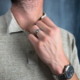 a man wearing a brushed silver titanium ring with a polished black inner sleeve holding his shirt collar