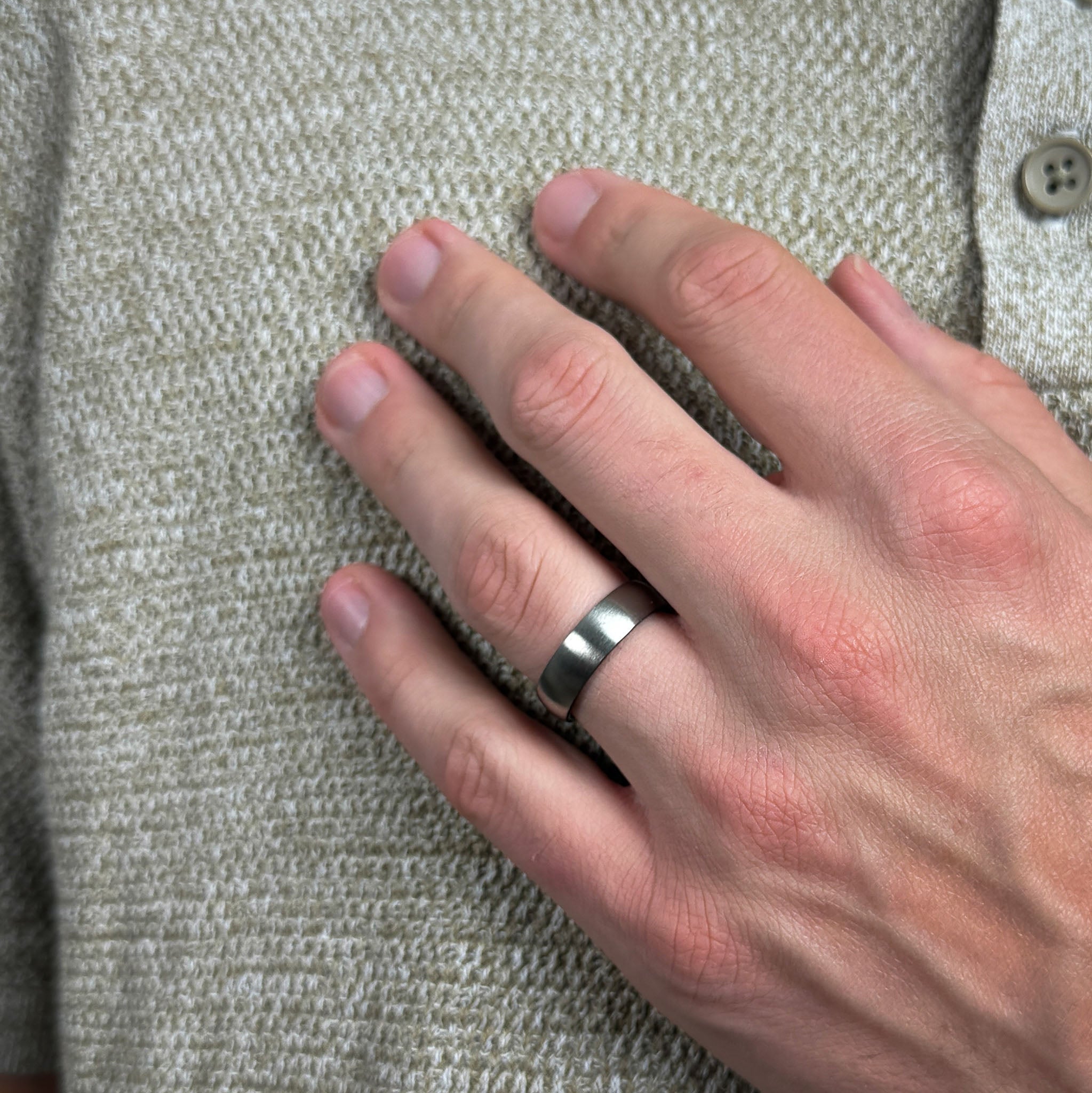 Hand wearing a silver ring on a textured fabric background