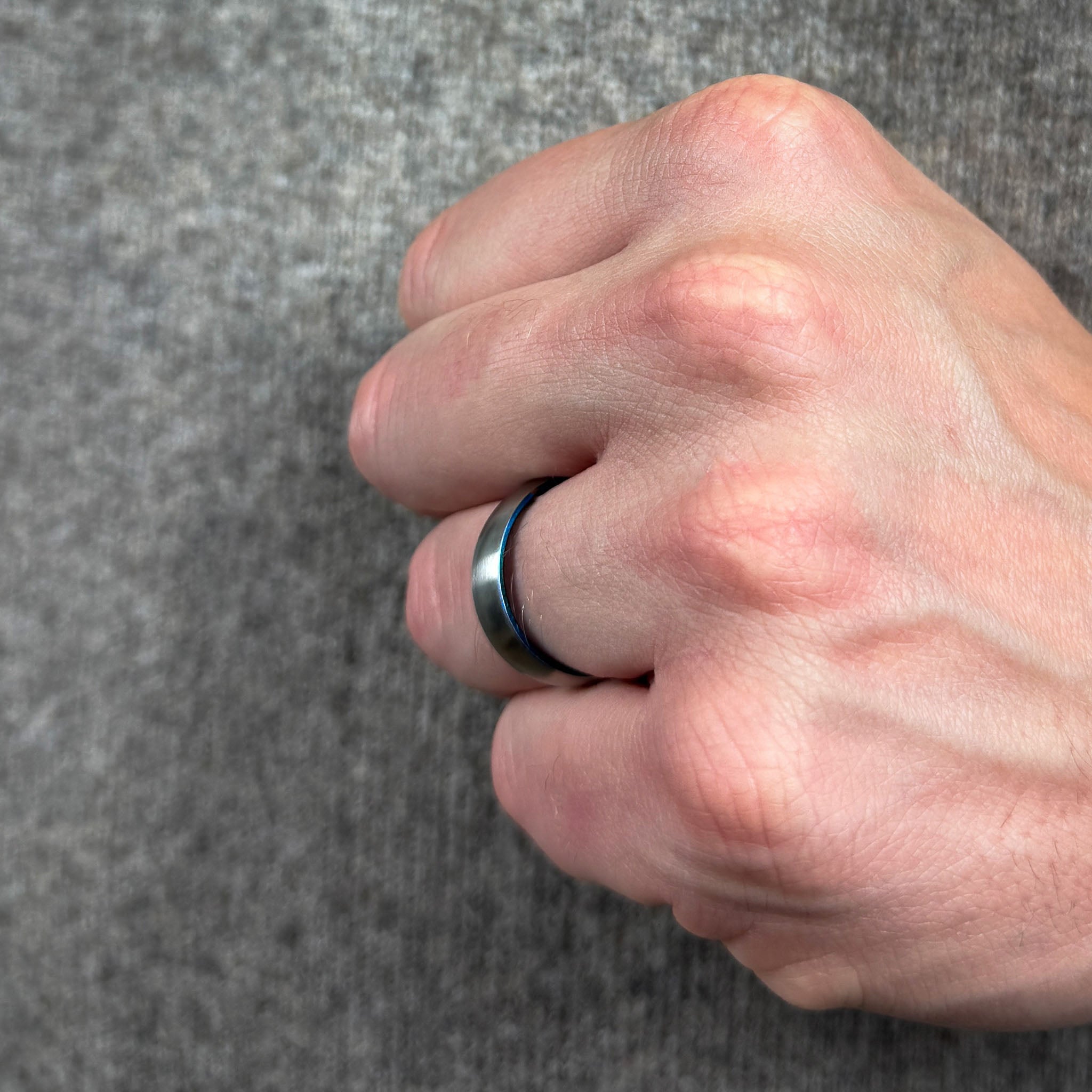 Hand wearing a silver and blue titanium ring on a gray background