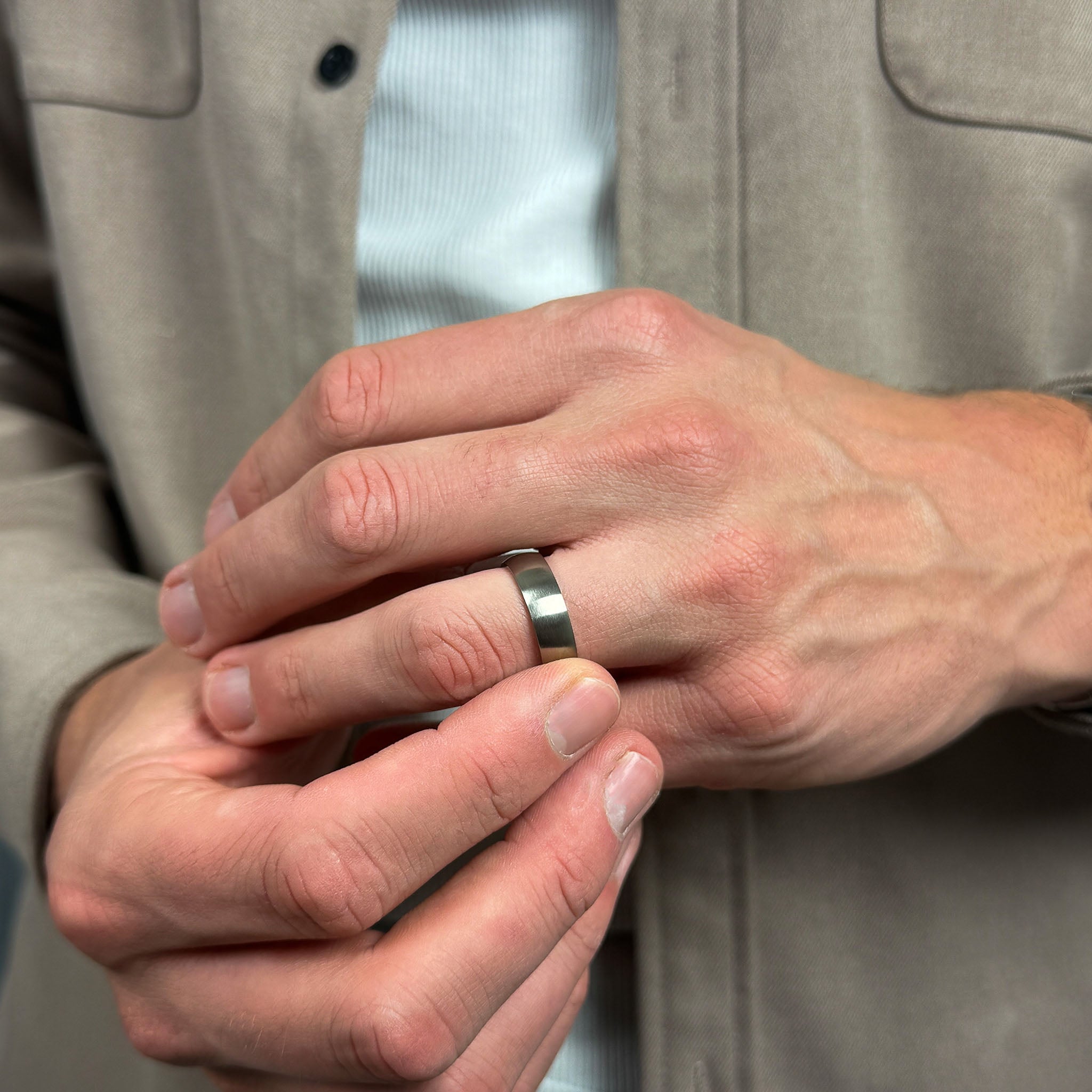 close up a mans hands wearing a brushed silver titanium wedding ring