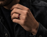 Close-up lifestyle photograph of a man wearing a silver tungsten wedding ring with red ruby inlay in a premium modern editorial setting.