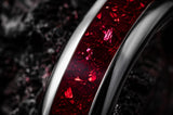 Ultra close-up macro photograph of a silver tungsten wedding ring with vivid red ruby inlay showing detailed gemstone texture and polished metal craftsmanship.