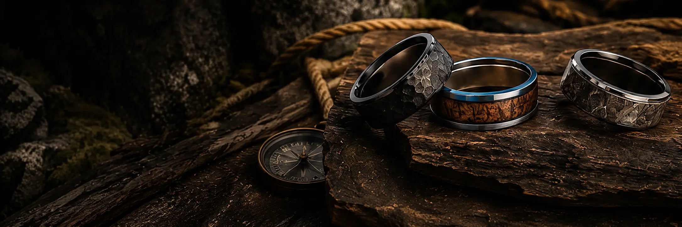 Rugged men's wedding rings displayed on weathered wood in an outdoor setting with rope, compass and natural textures.