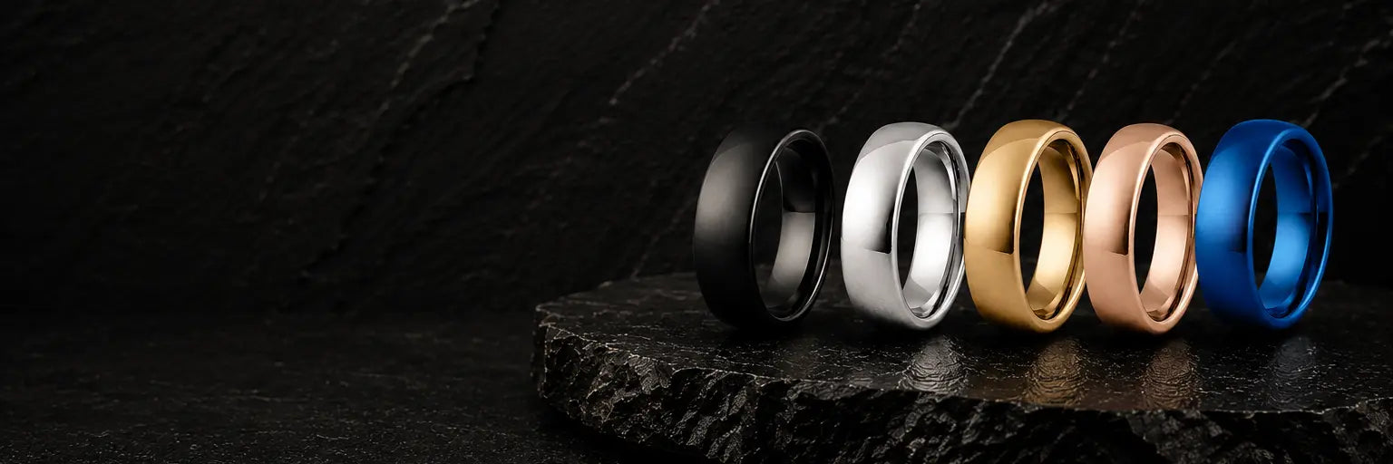 Black, silver, gold, rose gold and blue tungsten wedding rings displayed on dark slate stone, showcasing the range of men's wedding ring colours.