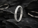 2mm silver dome wedding band resting on dark volcanic rock with moody cinematic lighting