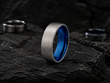 Silver and blue titanium wedding ring resting on dark volcanic rock in a premium masculine jewellery collection image