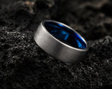 Ultra close-up macro photograph of a brushed silver titanium wedding ring with polished blue inner sleeve on volcanic rock textures
