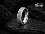 Silver brushed men’s wedding ring on dark volcanic rock with moody cinematic lighting and rugged slate textures