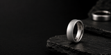 Polished silver dome tungsten wedding ring on dark slate stone with cinematic lighting and luxury masculine ecommerce styling