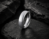 Close-up macro shot of a polished silver tungsten wedding ring on dark stone highlighting durability and smooth rounded edges