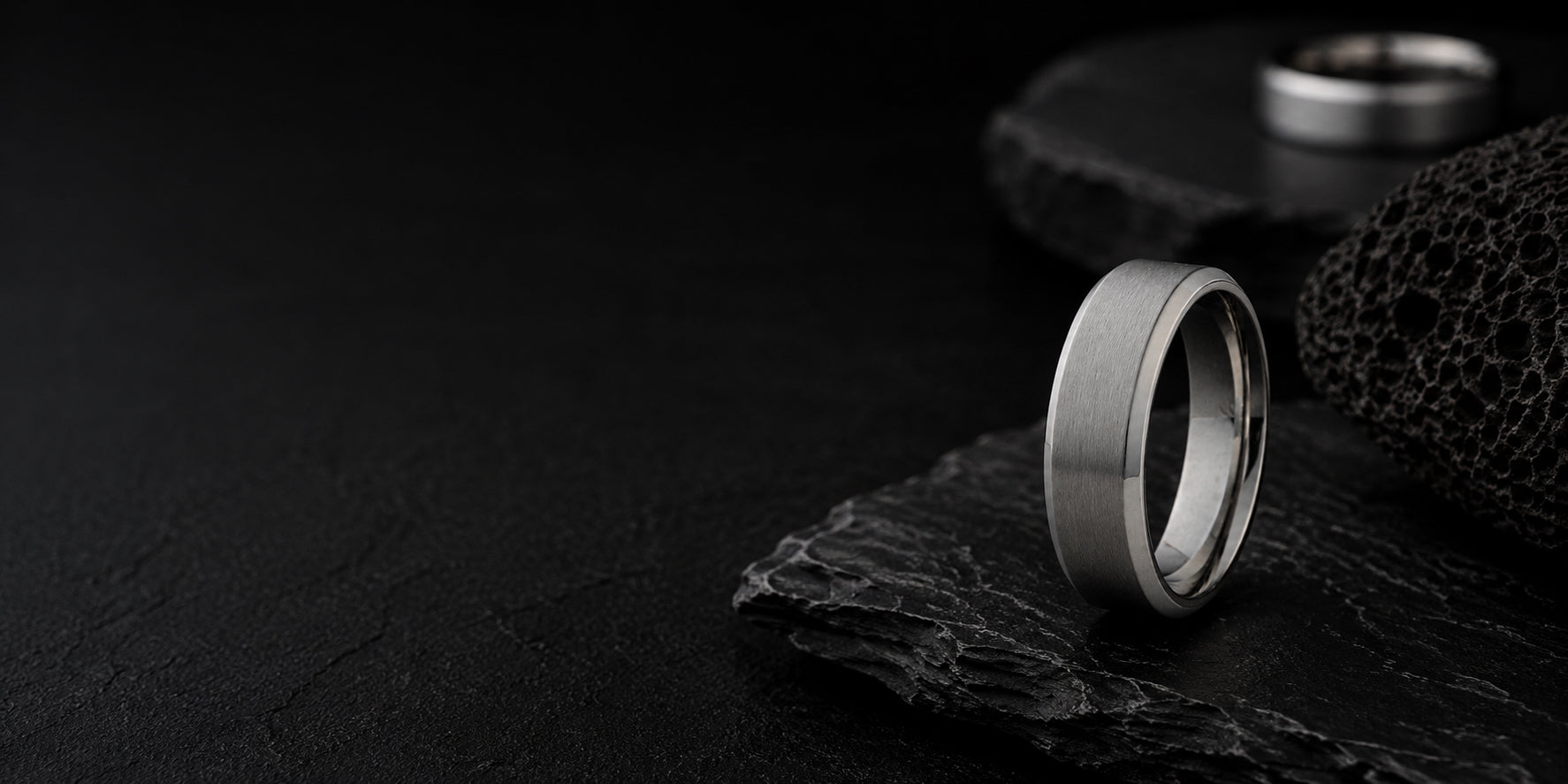 Premium cinematic hero banner featuring a brushed silver titanium men’s wedding ring against a dark textured slate background.
