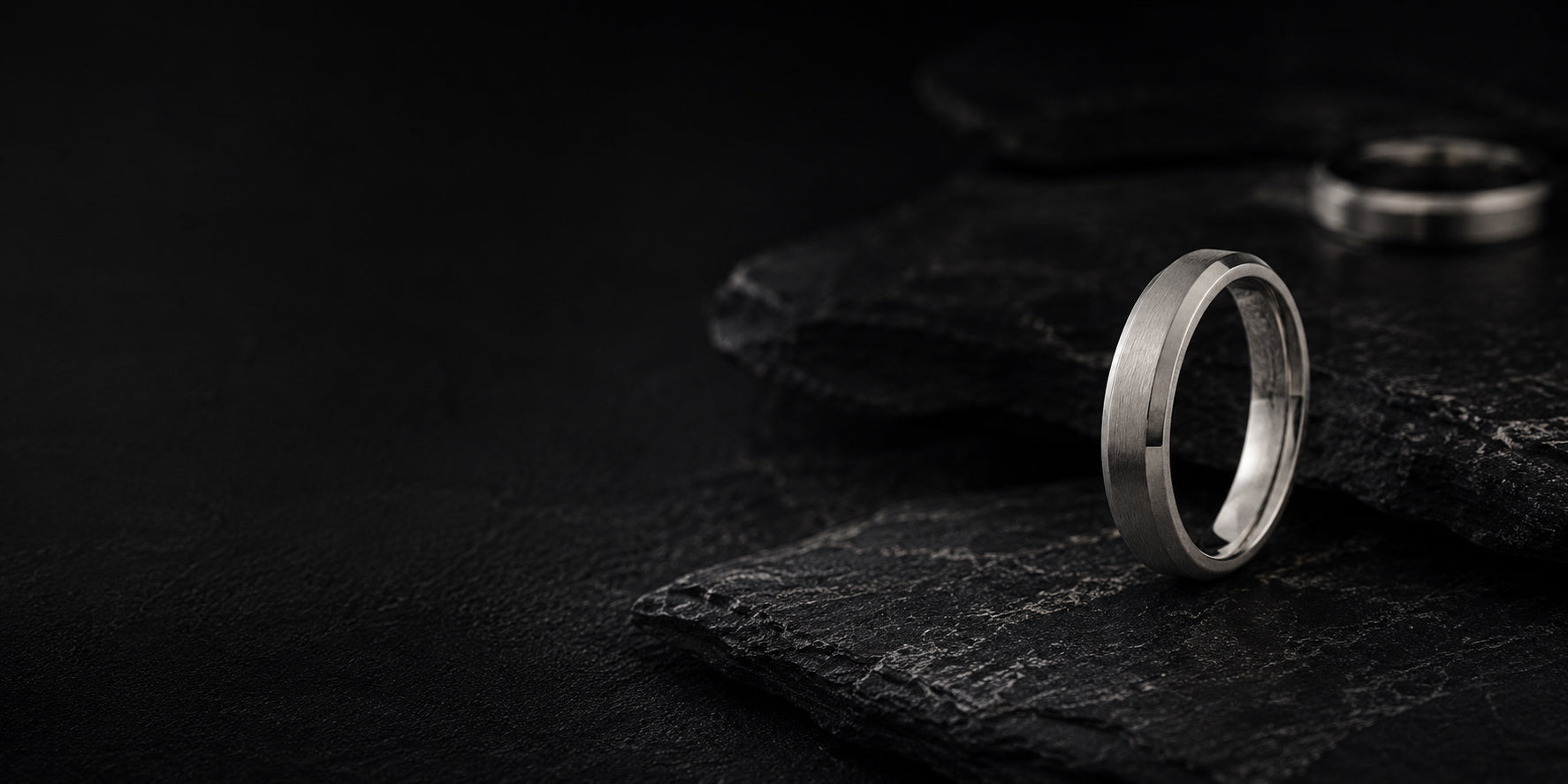 Silver titanium men’s wedding ring on dark volcanic slate with moody cinematic lighting
