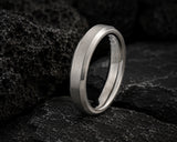 Macro close-up of a silver titanium men’s wedding ring on dark volcanic rock textures