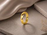 Women’s faceted gold wedding ring on soft neutral stone background with elegant feminine styling
