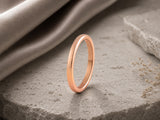 Rose gold women’s wedding ring standing on dark charcoal stone with soft luxury lighting for a premium wedding ring collection.